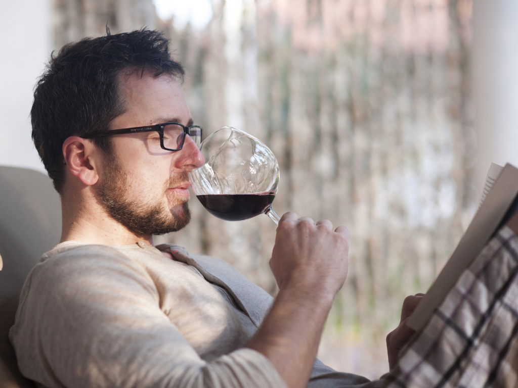 A man in a work shirt sitting alone reading a book with a glass of wine